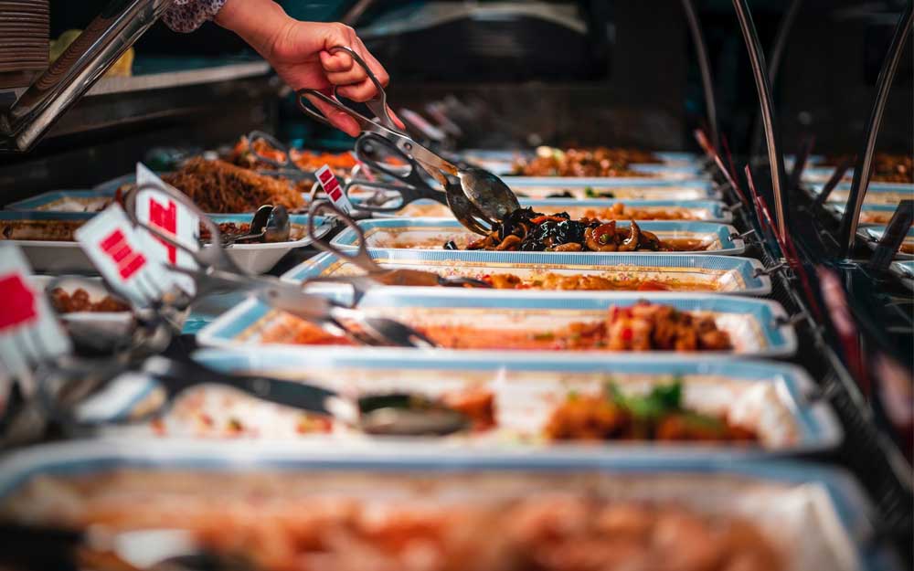 various dishes lined up in chafing dish with tongs to self serve the food